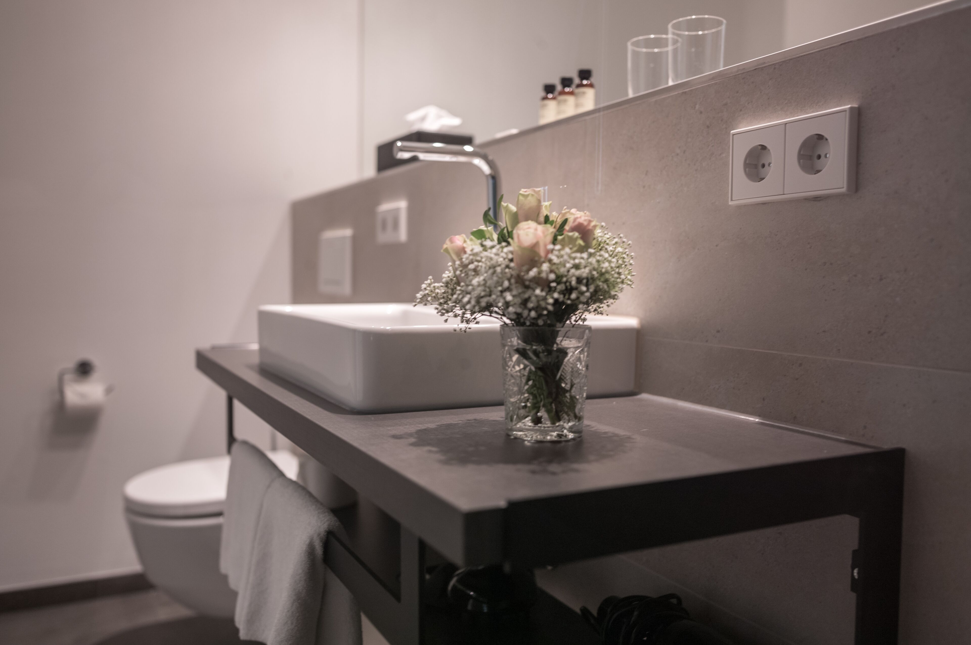 A bathroom with a white sink, a mirror, and a vase with flowers on the countertop.