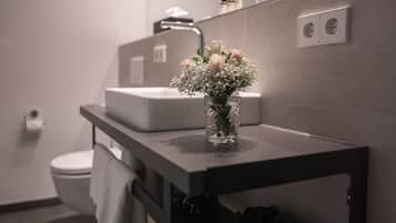 A bathroom with a white sink, a mirror, and a vase with flowers on the countertop.