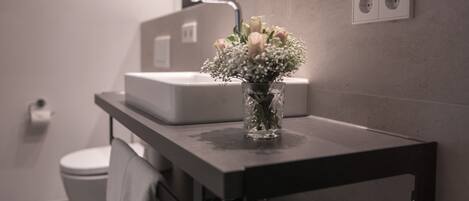 A bathroom with a white sink, a mirror, and a vase with flowers on the countertop.