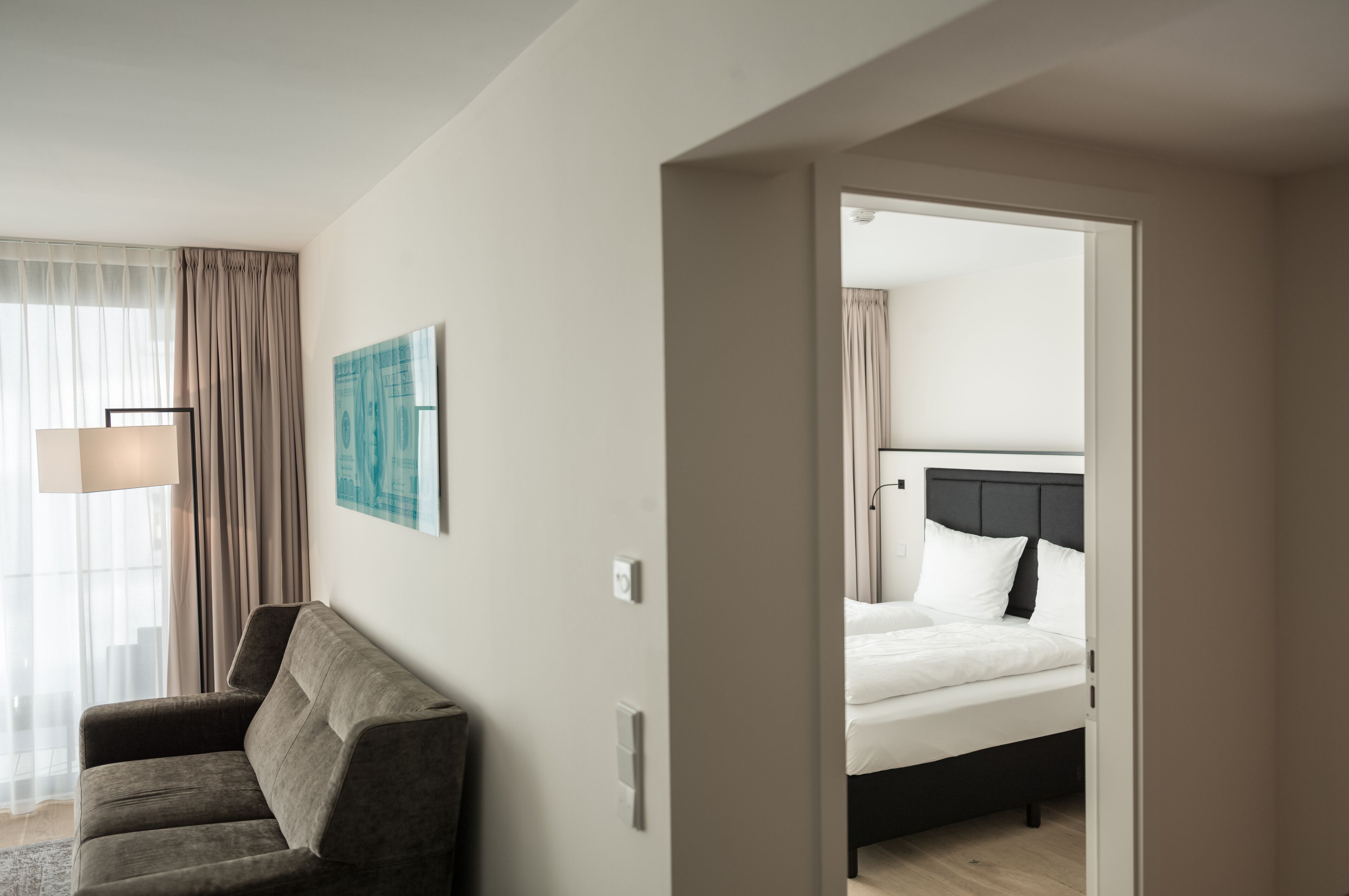 Habitación de hotel con cama, sofá, ventana con cortinas y lámpara de pared.