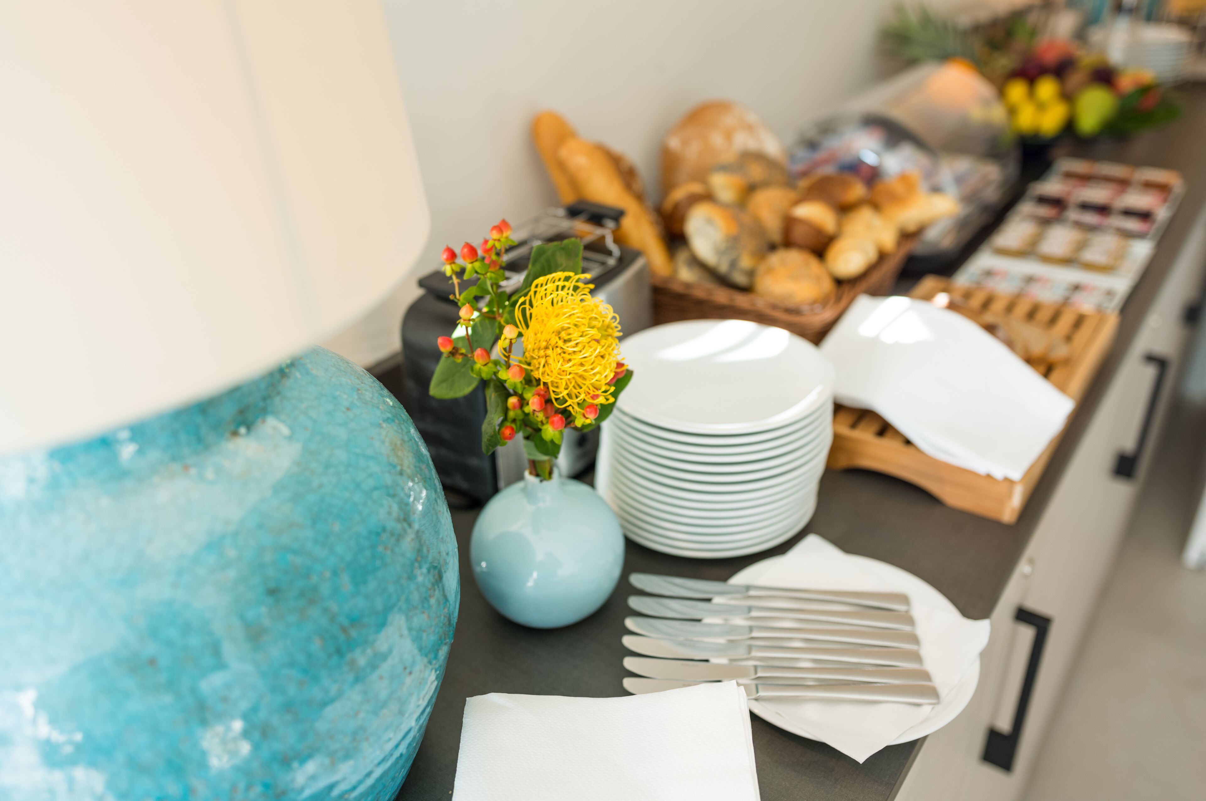 A breakfast buffet with various breads, pastries, and a vase with flowers.