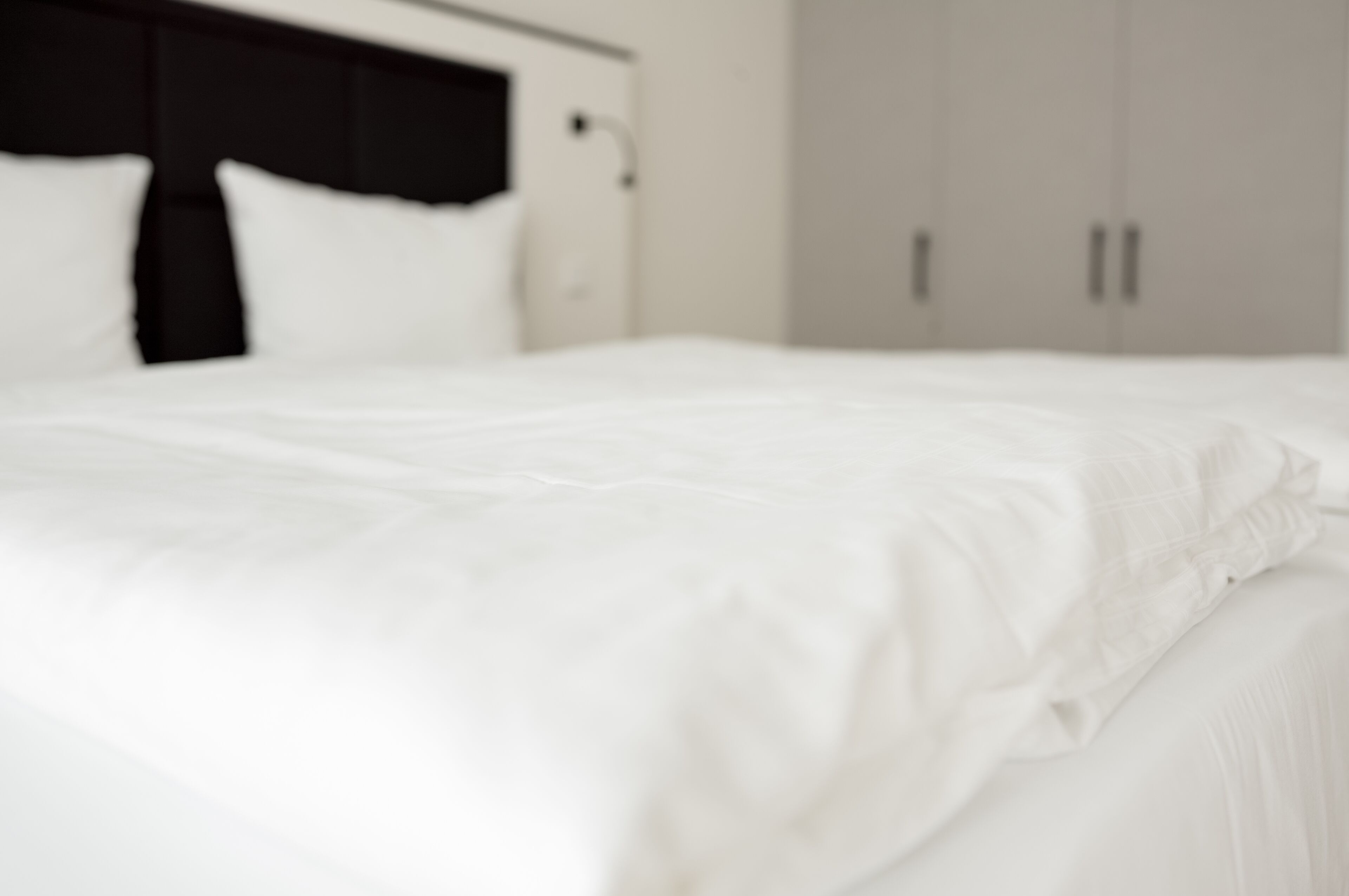 A neatly made bed with white linens in a hotel room.