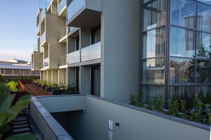 Un edificio moderno con varios balcones, un jardín en la azotea y ventanas amplias.