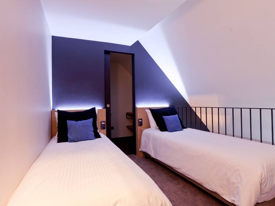 Una habitación pequeña y moderna con dos camas individuales, una puerta y un techo inclinado.