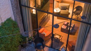 Une terrasse extérieure avec un sol en pierre, plusieurs coins salon comprenant des tables et des chaises, et une vue sur une pièce adjacente dotée d’une cheminée.