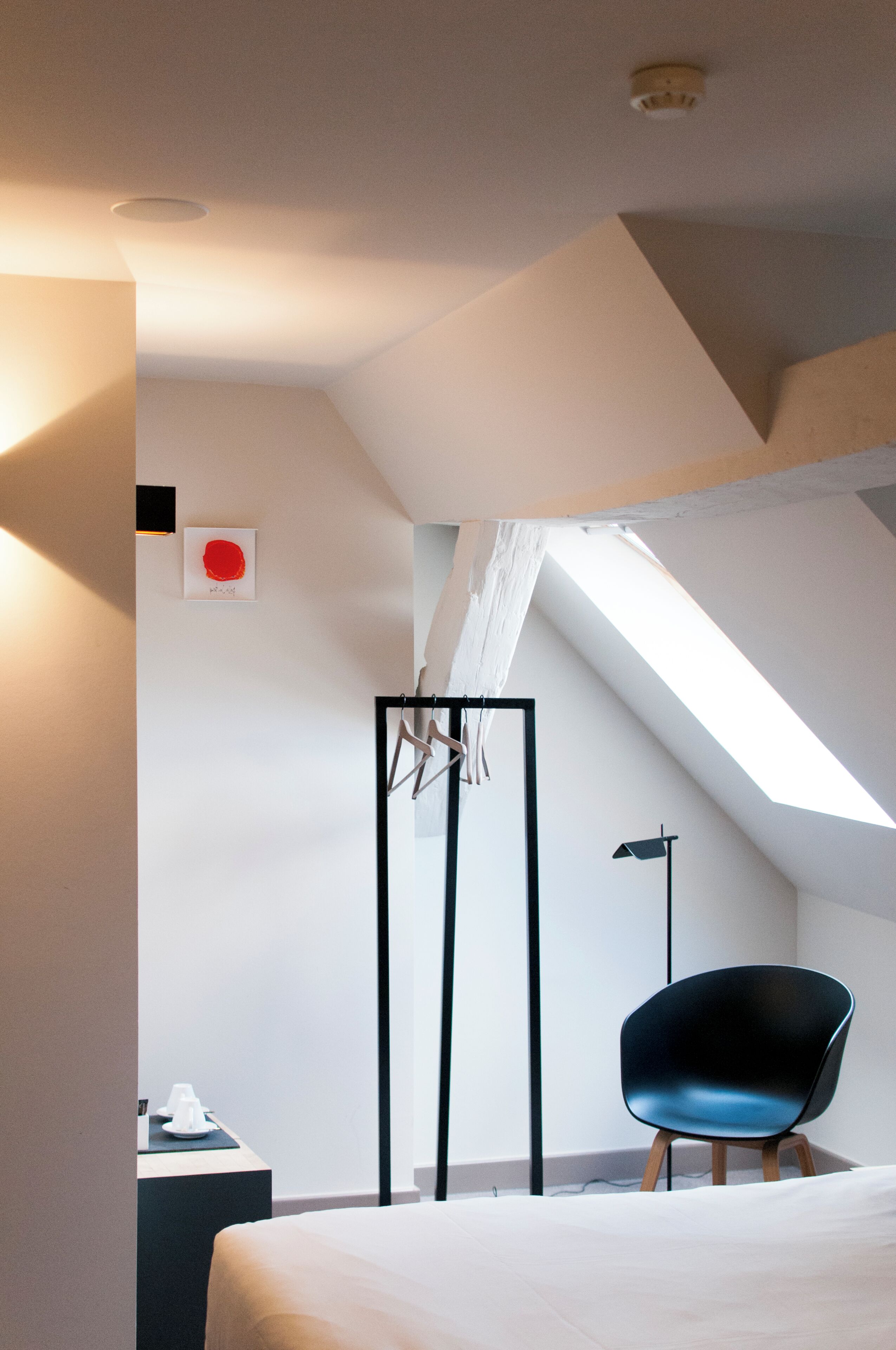 Un dormitorio moderno con techo inclinado, una cama, una silla y una mesita de noche.