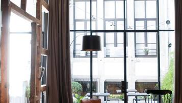 Una sala de estar moderna con un sofá negro, un sillón redondo también negro, y una mesa de centro de madera. Amplias ventanas con cortinas dejan entrar luz natural.