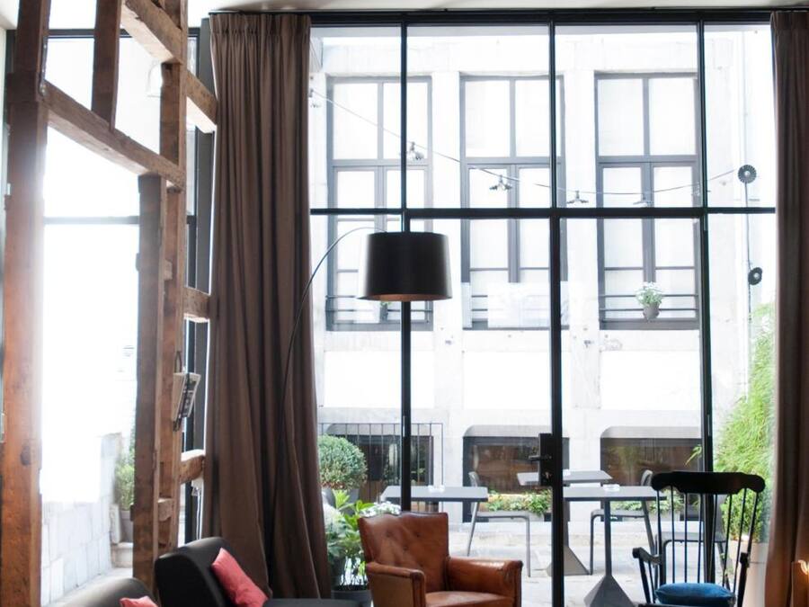 Una sala de estar moderna con un sofá negro, un sillón redondo también negro, y una mesa de centro de madera. Amplias ventanas con cortinas dejan entrar luz natural.