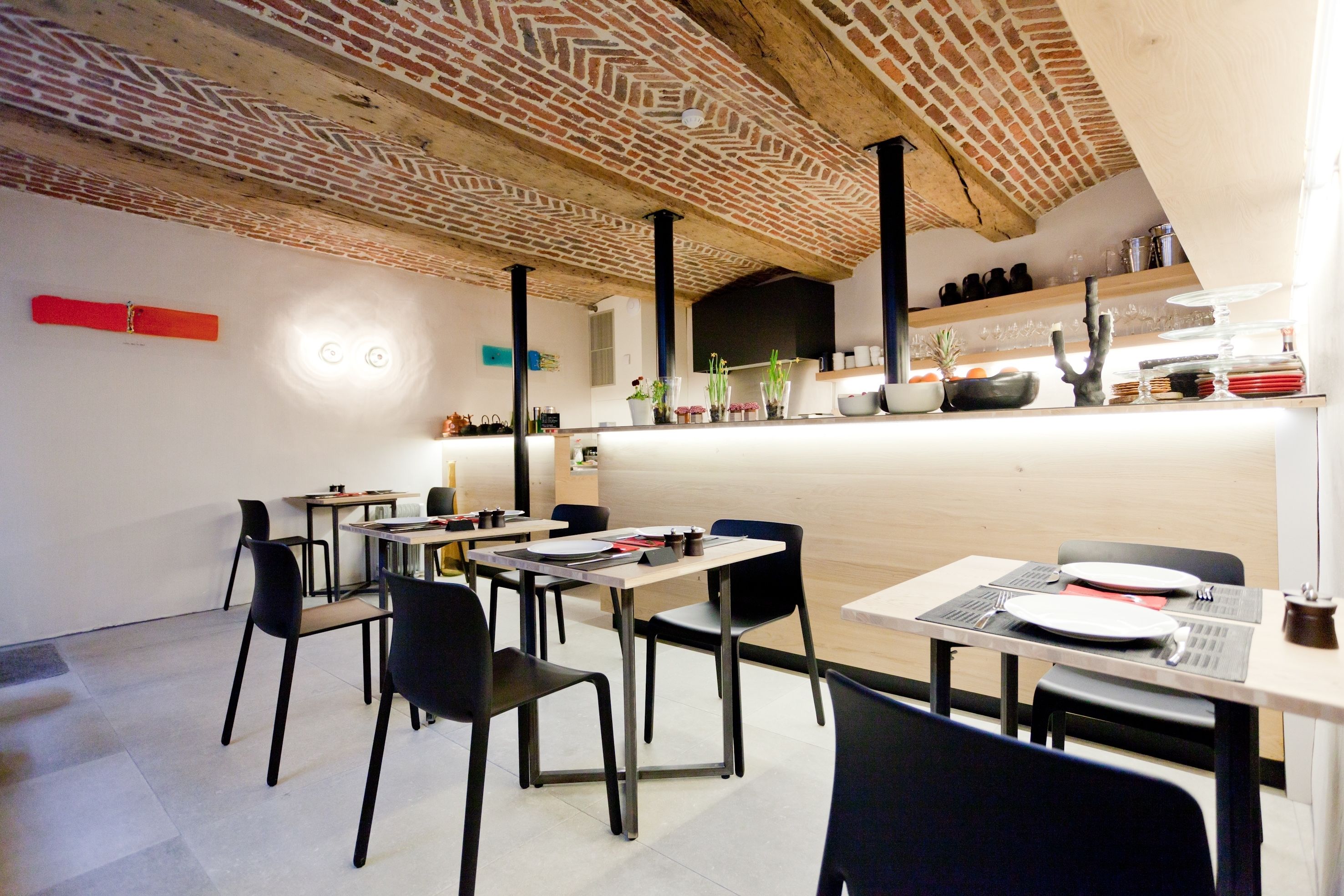 Un espace de restauration moderne avec un plafond en briques apparentes, des chaises noires et une longue table dressée avec des assiettes et des couverts.