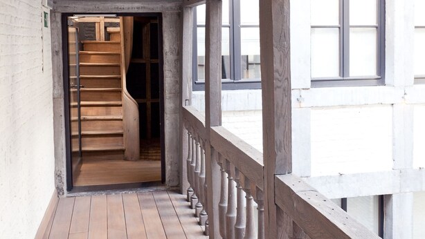 Un escalier en bois menant à l’étage supérieur, une balustrade en bois et une vue sur l’extérieur grâce à de grandes fenêtres.