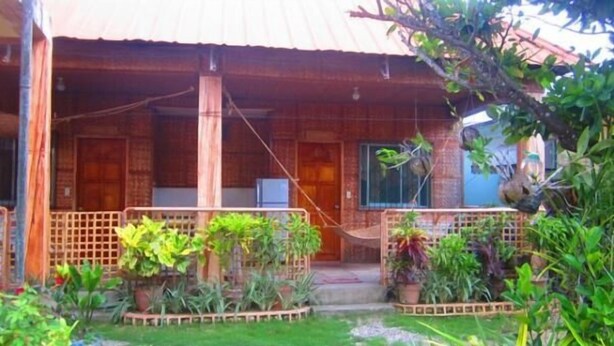 Una casa de madera con un porche cubierto, plantas en macetas y un pequeño jardín.