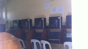 Un laboratorio de computadoras con varias computadoras de escritorio, sillas de plástico blanco y una mesa de madera.