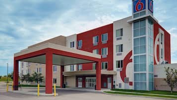 A modern hotel with a red and white facade, a covered entrance, and a prominent '6' sign on the roof.
