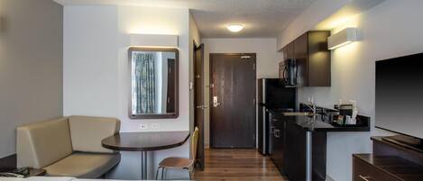 Habitación de hotel compacta con cama, una zona de estar pequeña, kitchenette y televisor.
