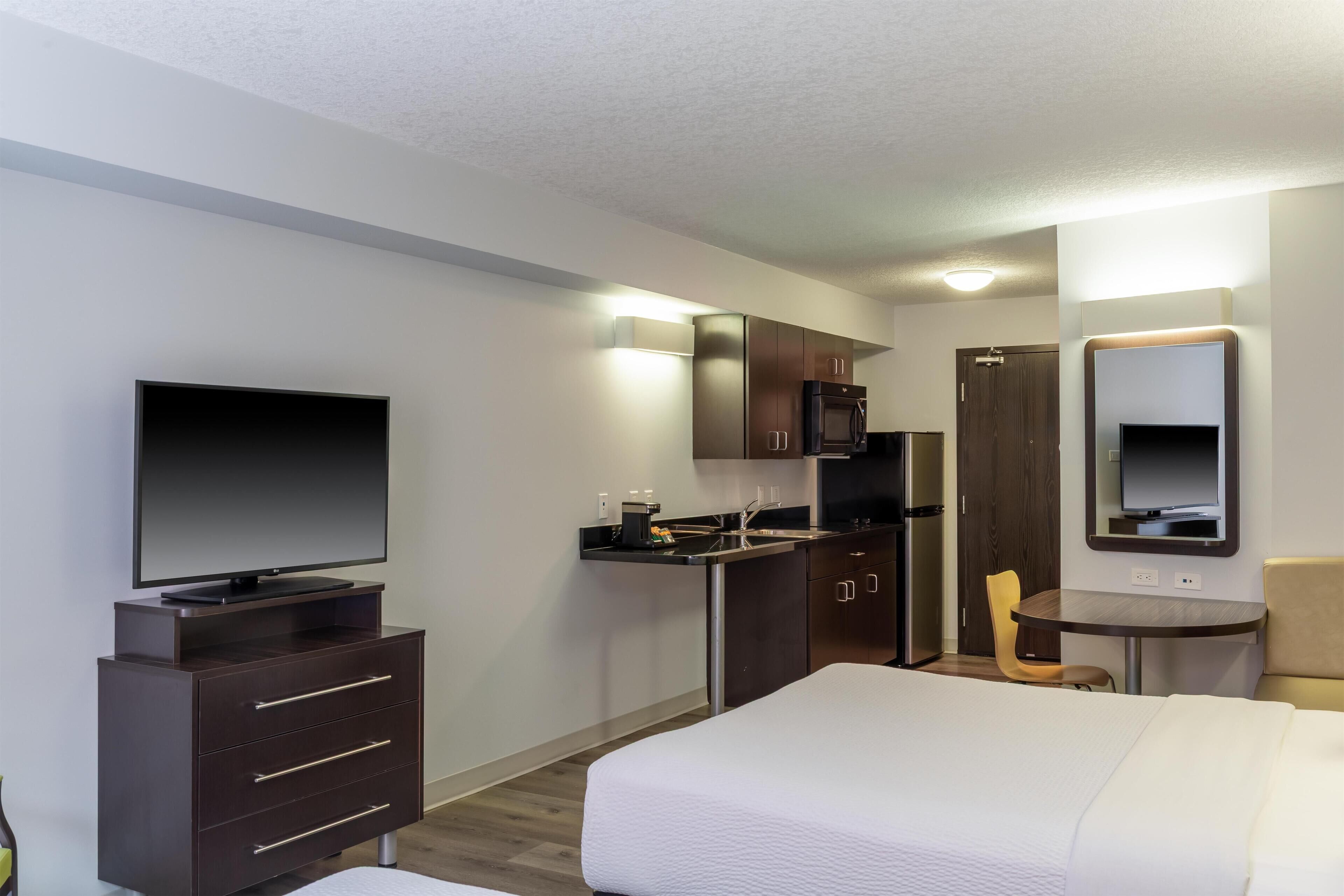 A hotel room with a bed, a TV, a desk, a chair, a microwave, and a refrigerator.