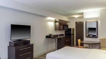 A hotel room with a bed, a TV, a desk, a chair, a microwave, and a refrigerator.