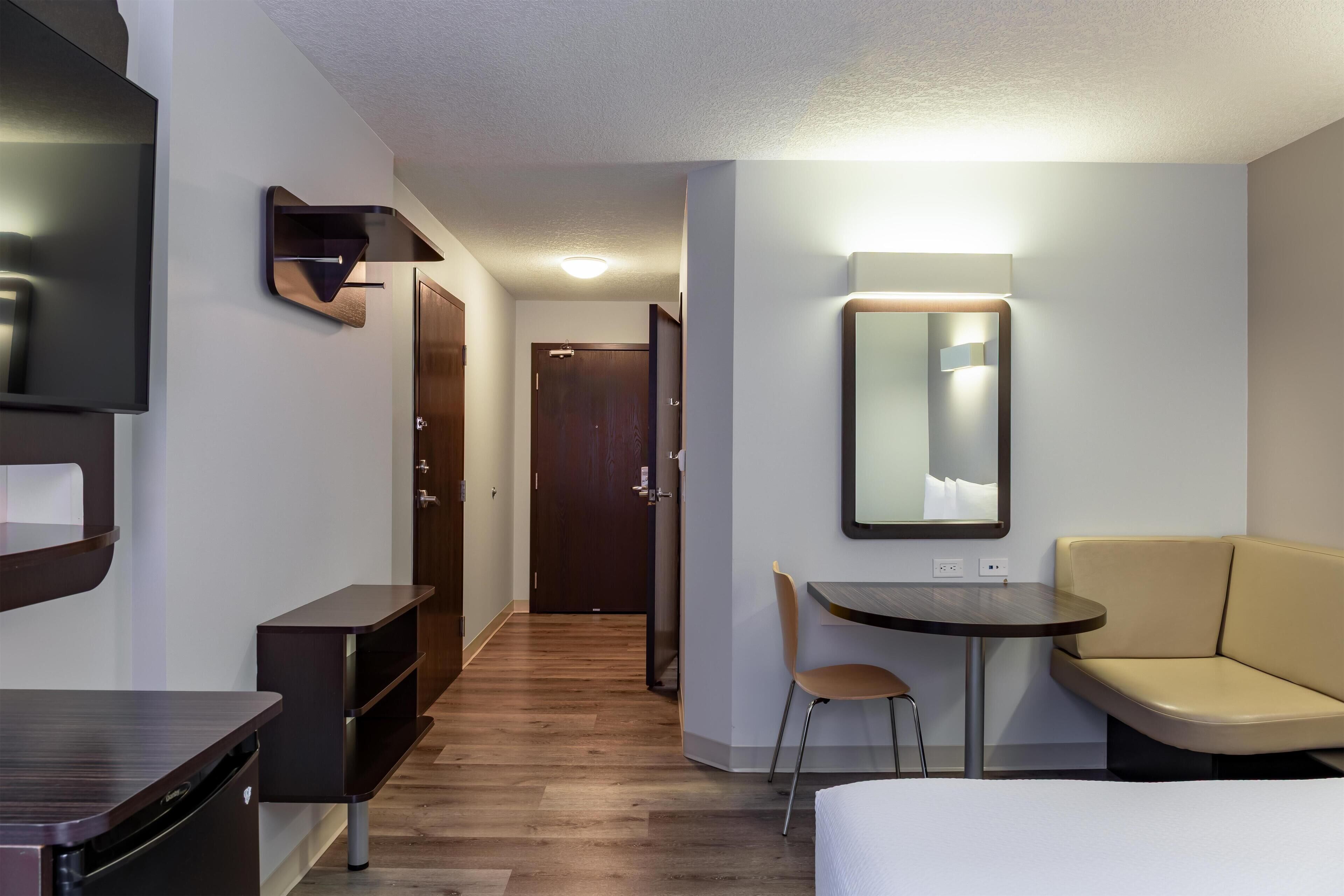Une chambre d’hôtel comprenant un lit, un bureau, une chaise, une télévision, un miroir et une porte donnant sur une autre pièce.