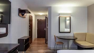 A hotel room with a bed, a desk, a chair, a TV, a mirror, and a door leading to another room.