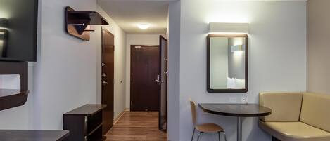 Une chambre d’hôtel comprenant un lit, un bureau, une chaise, une télévision, un miroir et une porte donnant sur une autre pièce.