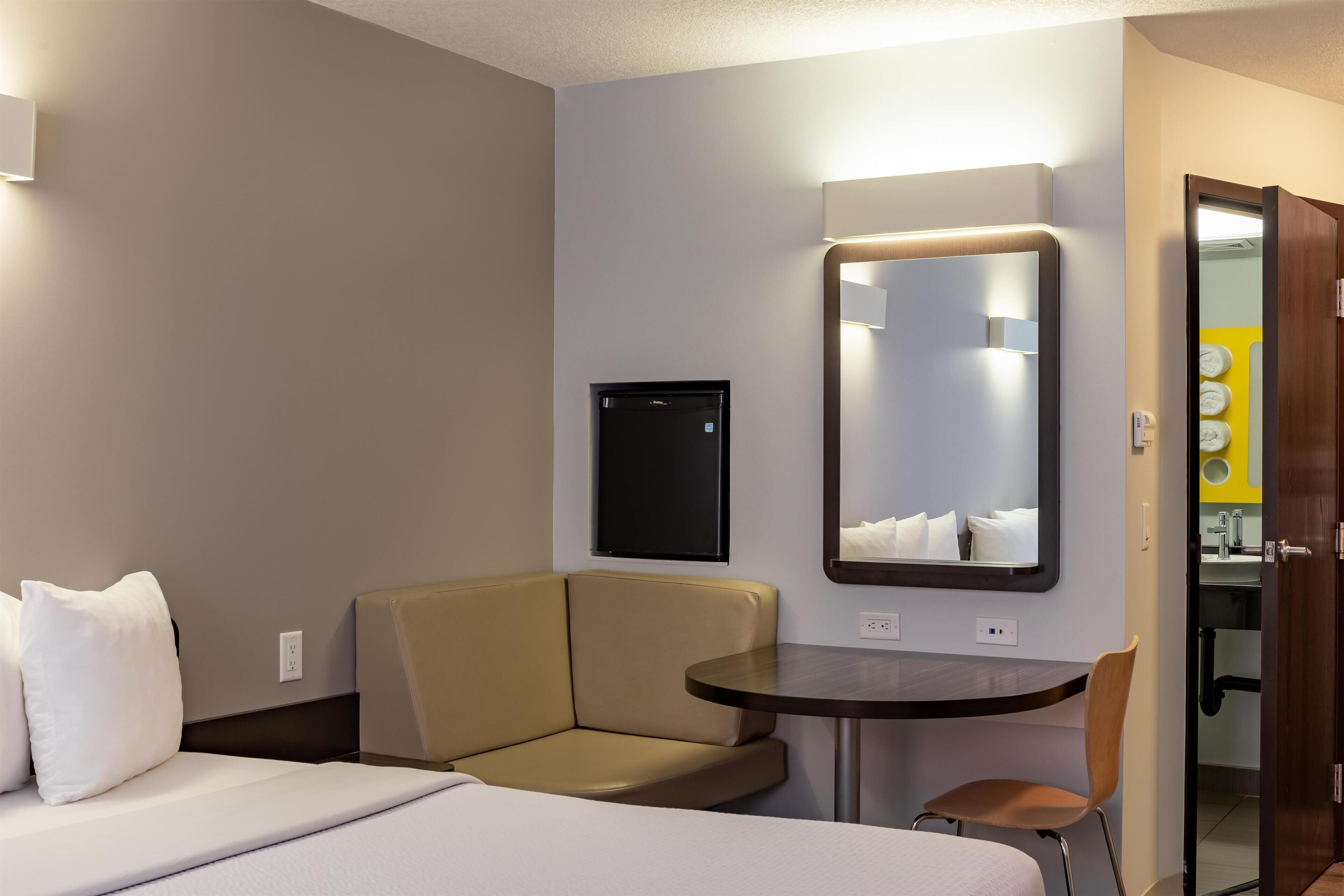 Een hotelkamer met een bed, een kleine zithoek, een rond tafeltje en een spiegel.