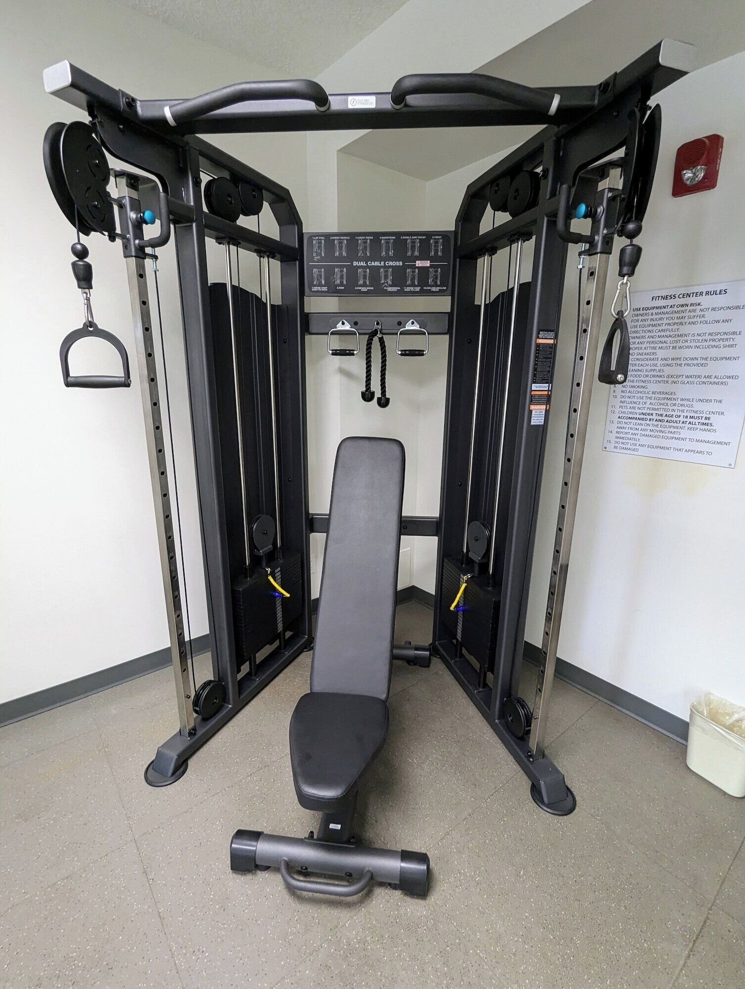 Une salle de sport équipée d’un banc de développé couché, de supports à poids et d’un panneau de commande fixé au mur.