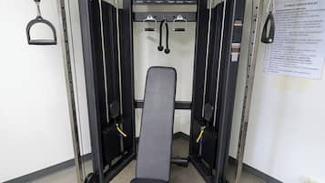 Une salle de sport équipée d’un banc de développé couché, de supports à poids et d’un panneau de commande fixé au mur.