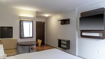 Una habitación de hotel moderna con una cama, un escritorio, una silla, un televisor montado en la pared y un ventanal con cortinas.