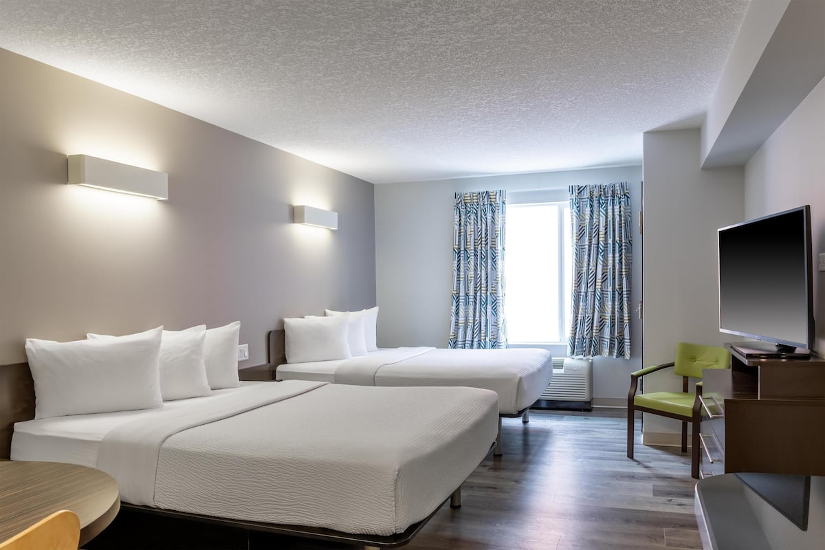Une chambre d’hôtel avec deux lits, un bureau, une télévision et une fenêtre avec des rideaux à motifs.