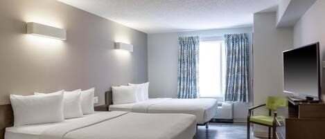 A hotel room with two beds, a desk, a television, and a window with patterned curtains.