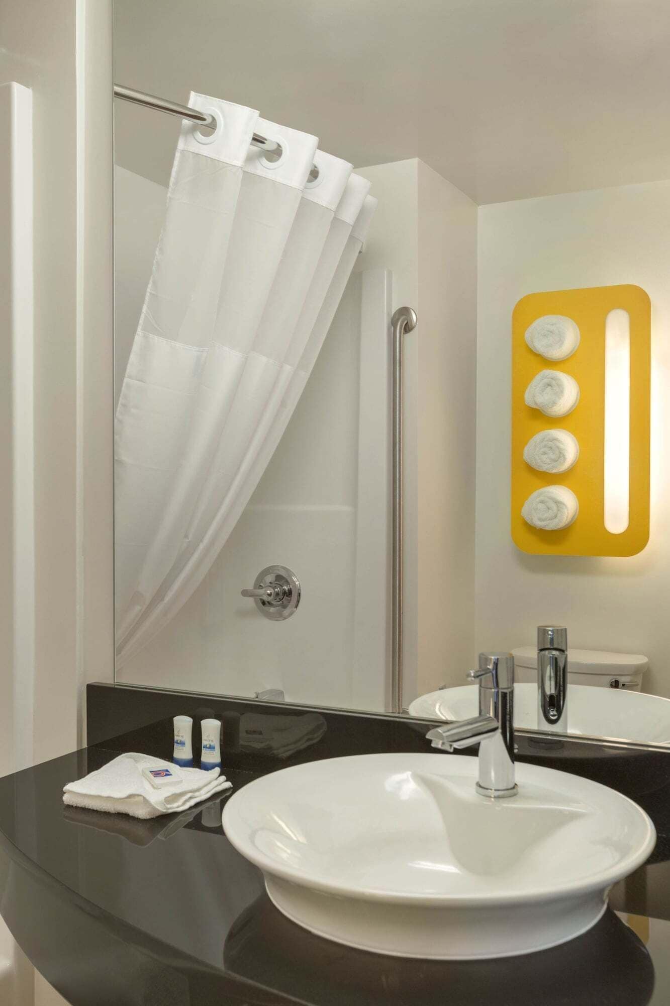 A modern bathroom with a glass shower enclosure, a white sink, and a mirror with a yellow light.