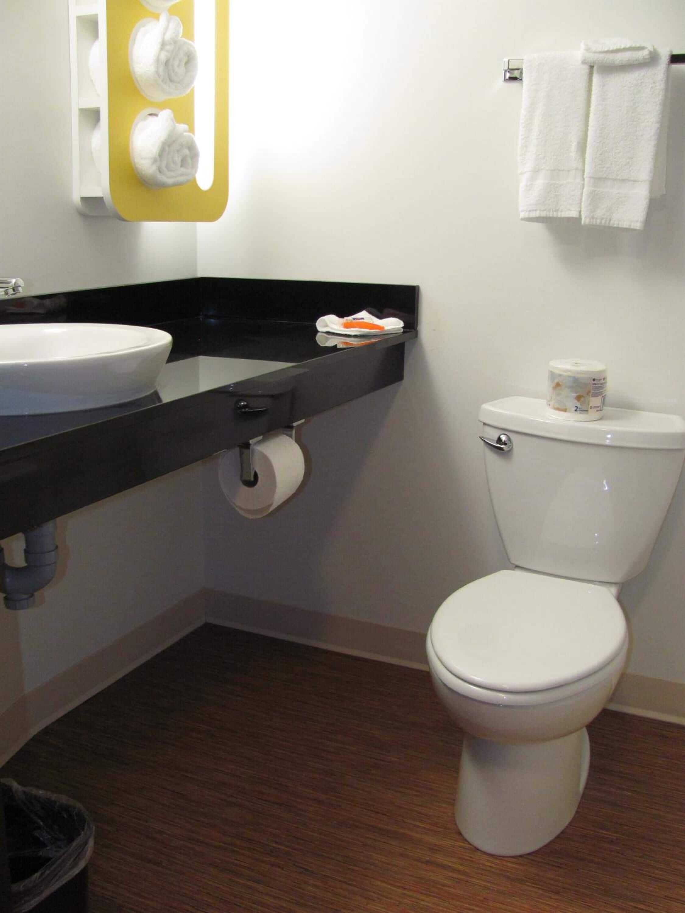 A bathroom with a white sink, black countertop, toilet, and a towel rack with two white towels.