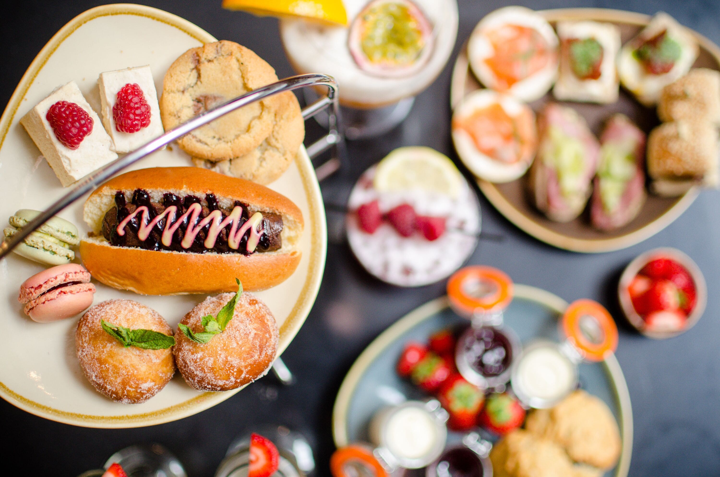 Una variedad de postres y pasteles en una mesa, como galletas, macarons y un pastel cubierto de chocolate.
