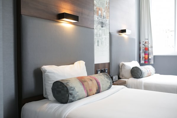 A hotel room with two beds, a nightstand, a wall-mounted light, and a window with curtains.