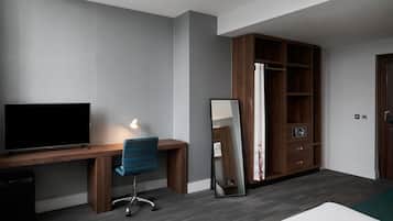 Una habitación moderna con un escritorio de madera, una silla, televisor de pantalla plana, un espejo y un armario.
