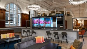 A bar area with a bar counter and stools, a seating area with sofas and a pool table, and a view of the city through large windows. - Aloft by Marriott Liverpool (Liverpool)