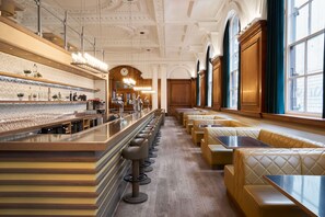 A bar area with a long counter, multiple stools, and seating with tables.