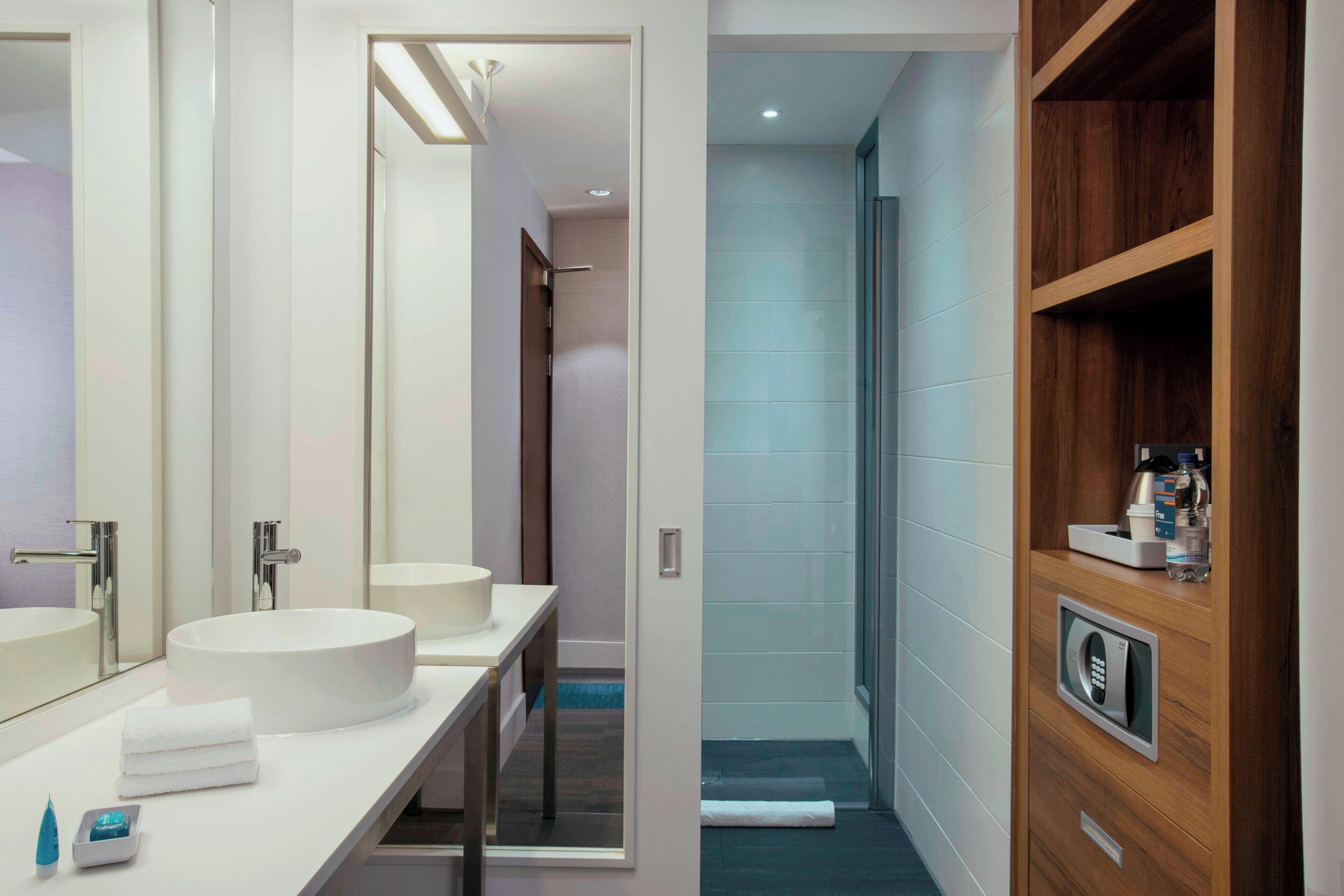 A modern bathroom with a vanity, two sinks, a mirror, and a shower area.