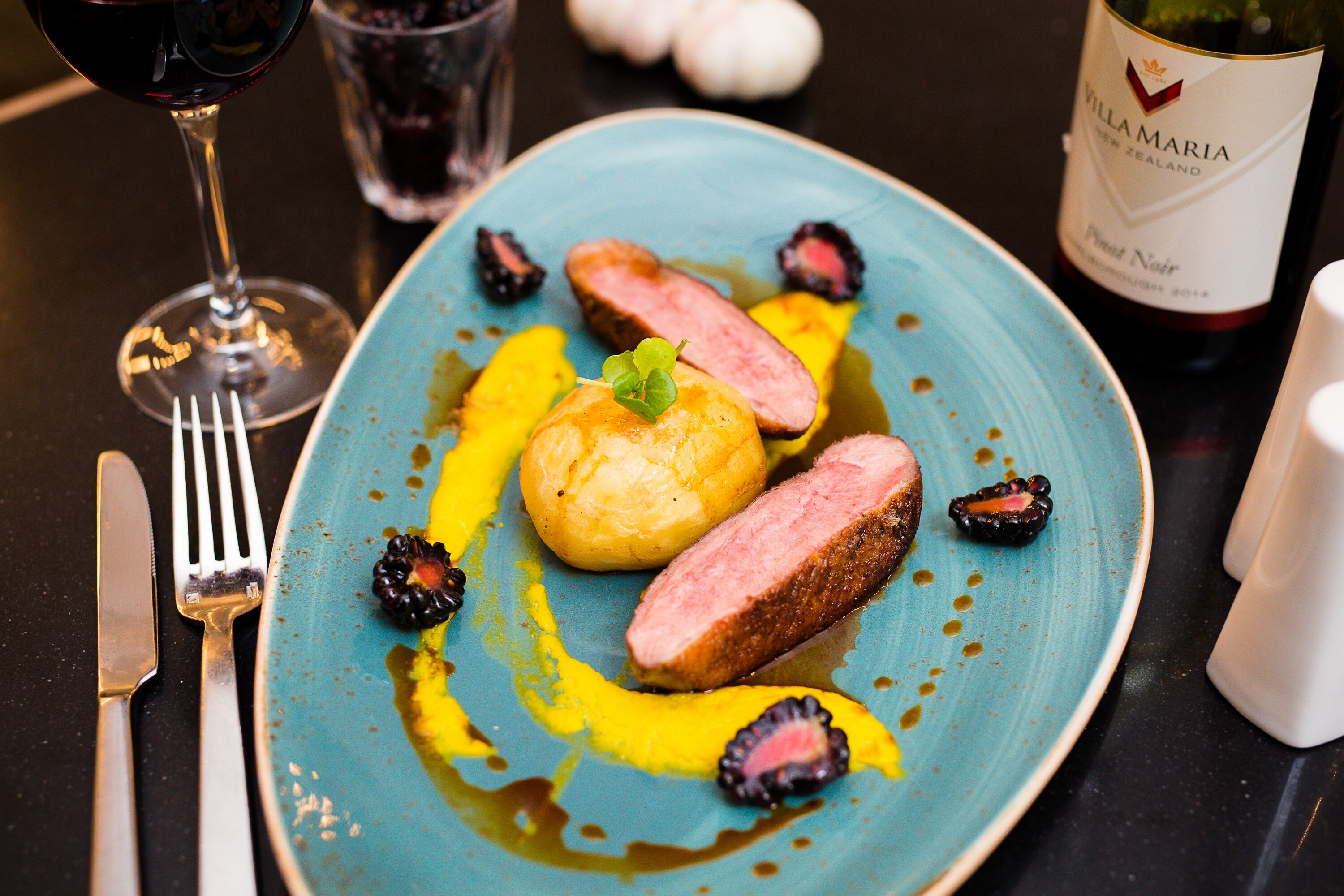 A plate of food with a bottle of wine and a glass of red wine on a table.