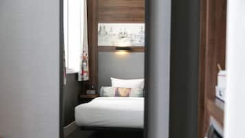 Un pasillo estrecho que conduce a una cama con vista a la ciudad, una mesita de noche y una lámpara.
