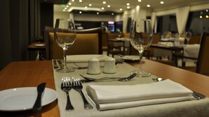 Una mesa de comedor dispuesta con un plato blanco, cubiertos y dos copas de vino, con una servilleta doblada sobre la mesa.