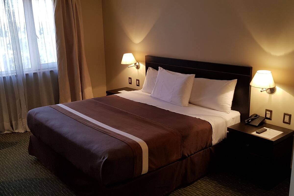 Habitación de hotel con una cama grande, dos lámparas de noche, un escritorio con teléfono y un ventanal con cortinas.