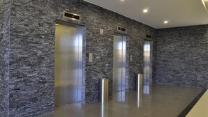 Un área de ascensores moderna con paredes de textura de piedra y puertas de metal.