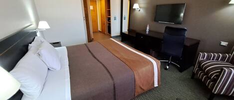 A hotel room with a bed, a desk, a chair, a TV, and a bathroom visible through an open door.