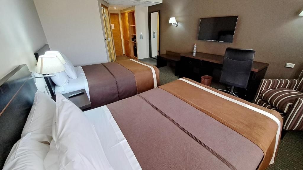 Una habitación de hotel con dos camas, un escritorio, una silla, un televisor y una lámpara.