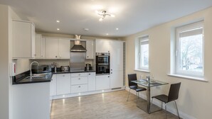 Una cocina moderna con armarios blancos, electrodomésticos de acero inoxidable y una mesa de vidrio con dos sillas.