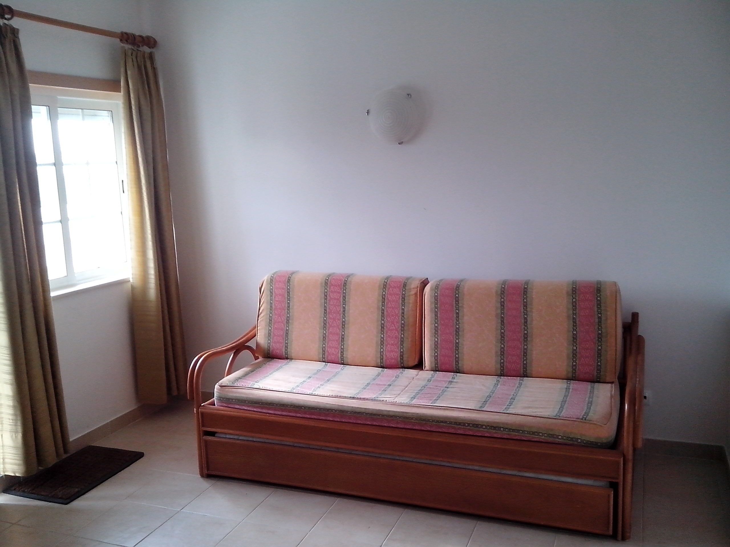 A wooden sofa with a striped cushion in a room with a window and curtains.