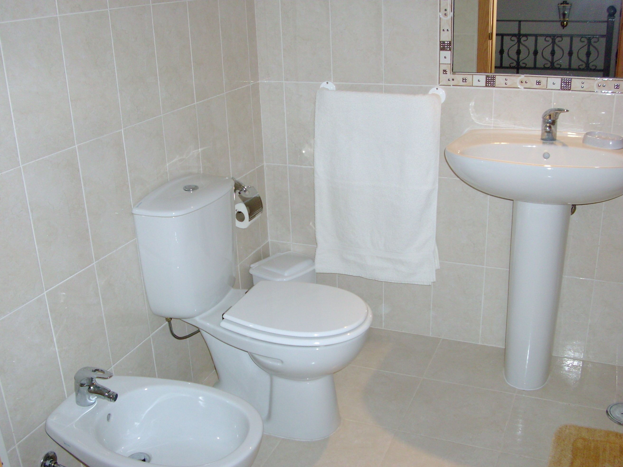 Et badeværelse med toilet, bidet, vask og et håndklæde hængende på væggen.