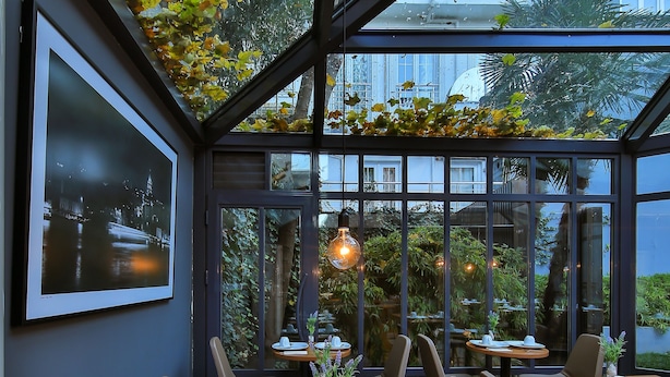 Ein Restaurant mit Glasdecke, Tische gedeckt mit weißen Tellern und Servietten, und Stühle mit Holzbeinen.