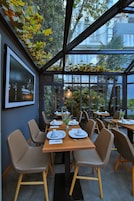 Un restaurante con techo de vidrio, mesas dispuestas con platos y servilletas blancos, y sillas con patas de madera.