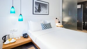 Ein modernes Hotelzimmer mit einem ordentlich bezogenen Bett, einem Nachttisch mit Telefon und Wasserkocher sowie einem gerahmten Bild an der Wand.